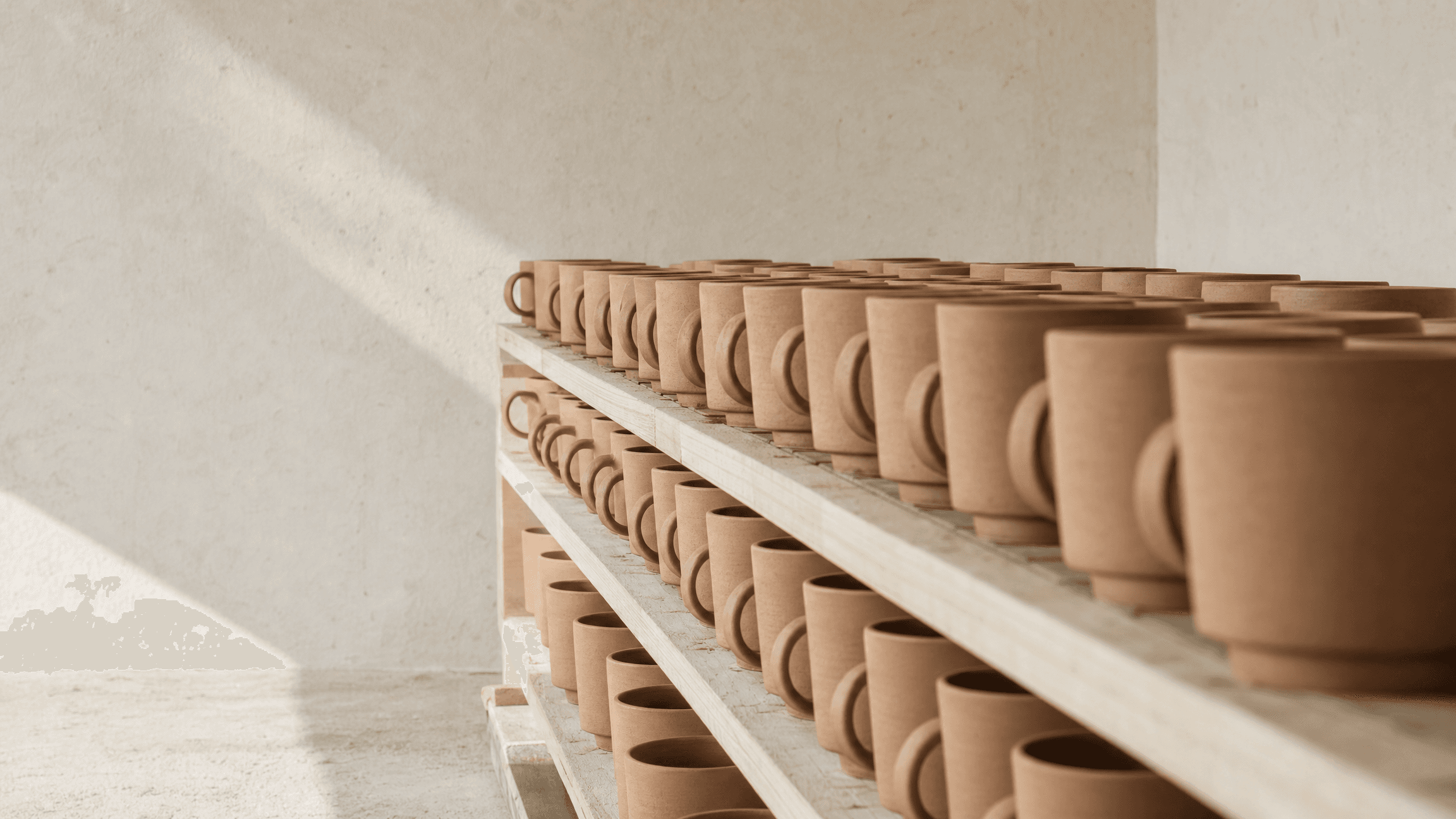 Rows of identical hand-thrown terracotta mugs drying on timber shelves
